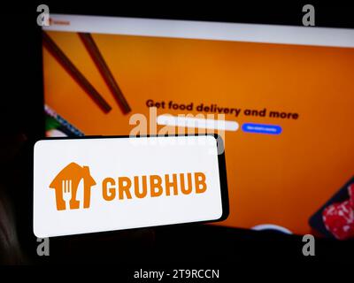 Person holding cellphone with logo of US food ordering and delivery company Grubhub Inc. in front of business webpage. Focus on phone display. Stock Photo