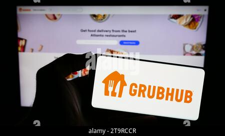 Person holding mobile phone with logo of American food ordering and delivery company Grubhub Inc. in front of web page. Focus on phone display. Stock Photo