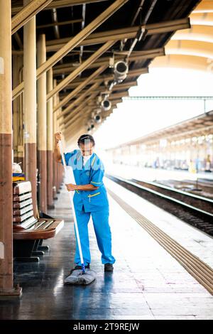 A female Thai cleaner makes her way along the platform mopping and sweeping the dirt and dust in Hua Lamphong Train station, Bangkok, Thailand. Stock Photo