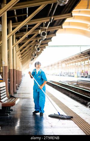 A female Thai cleaner makes her way along the platform mopping and sweeping the dirt and dust in Hua Lamphong Train station, Bangkok, Thailand. Stock Photo