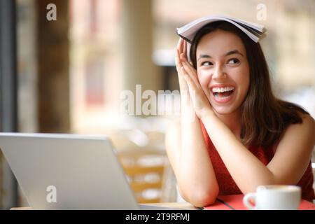 Joyful student joking with a notebook in her head looking at side in a restaurant Stock Photo