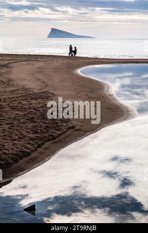 A couple walking on the beach with the island  in the background Stock Photo