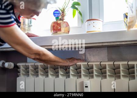 Senior woman checking temperature on a heating radiator in the kitchen at home Stock Photo