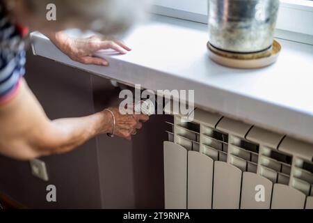 Senior woman checking temperature on a heating radiator in the kitchen at home Stock Photo