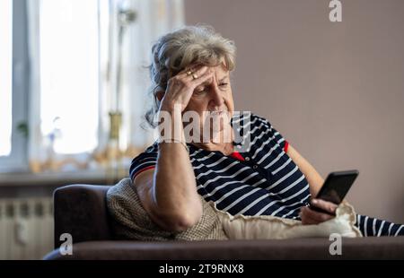 Elderly woman sitting on couch and using mobile phone at home Stock Photo