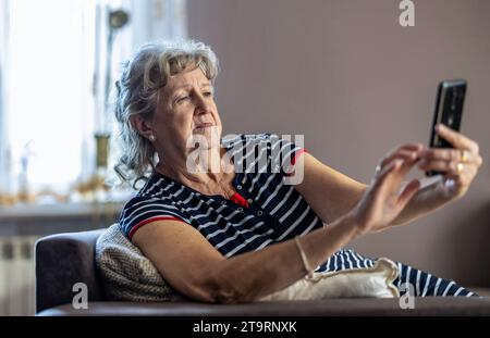 Elderly woman sitting on couch and using mobile phone at home Stock Photo
