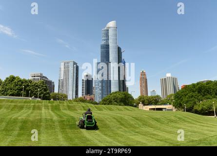 Worker mowing grass in The Great Ivy Lawn at The Field Museum Park with Chicago skyscrapers at the background. Stock Photo