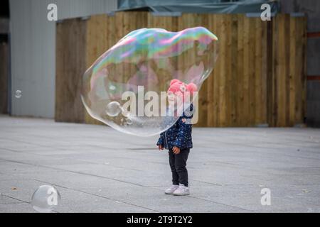 child looking at large soap bubbles near the cathedral, Cologne, Germany.   ###EDITORIAL USE ONLY###    Kind bestaunt grosse Seifenblasen nahe Dom, Ko Stock Photo