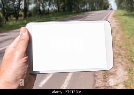 A man holds a tablet in his hand on the background of the road, a concept on the topic of finding a route, a template for the designer Stock Photo