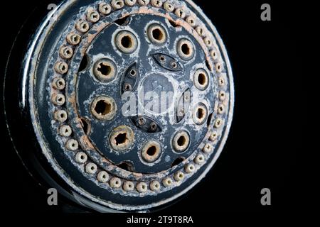 Hard water calcium or lime scale deposits on old, worn out shower head. Close up studio shot, isolated on black, no people. Stock Photo