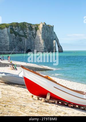 A red boat standing on the seashore with elephant like sea cliff in the background in Étretat Stock Photo