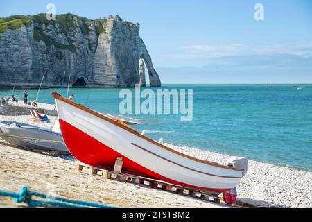 A red boat standing on the seashore with elephant like sea cliff in the background in Étretat Stock Photo