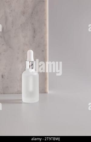 Fashionable beauty product in white matte bottle with dropper on marble flat stone background. A copy of the space. Front view. Empty packaging for th Stock Photo