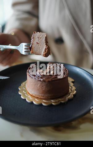 Chocolate cheesecake on Black plate, Woman holding a fork with a piece of cheesecake on it. Stock Photo