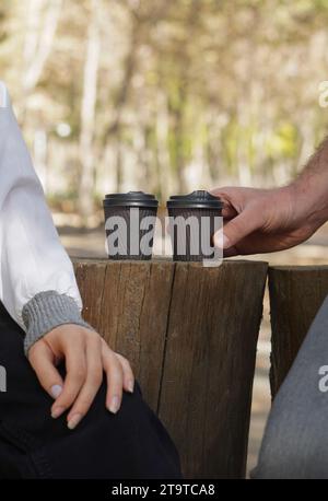 wo paper coffee cups on a tree stump, a man is gripping in cup in his hand Stock Photo