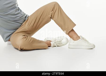 man wearing white sneakers and beige pants sitting on floor Stock Photo