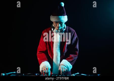 Cheerful club DJ in Santa outfit mixing music on a Christmas party in nightclub Stock Photo