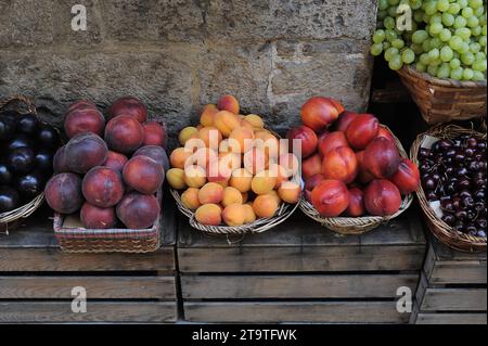 Baskets of fresh peaches, plums, apricots, cherries, grapes and nectarines set on wooden crates in a produce market in Italy. Stock Photo