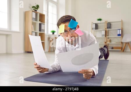 Funny business man doing plank exercise on yoga mat on the floor in office. Stock Photo