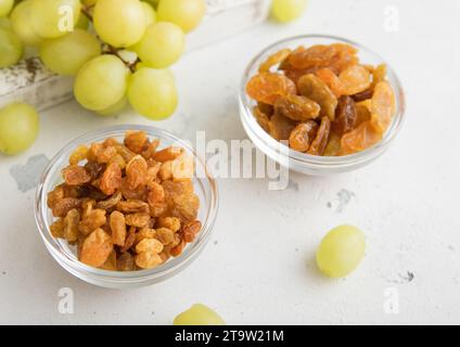 Sweet dried green raisins in glass bowl with ripe grapes in wooden box on light kitchen background.Macro Stock Photo