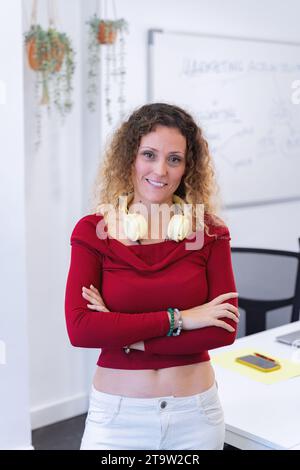 Woman with headphones posing with her arms crossed in the office. Business concept. Stock Photo