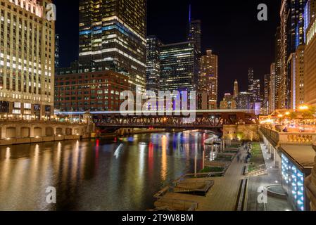 Nigh view of Chicago downtown and river. Light trails left by a passing train are visible on the bridge in foreground. Stock Photo