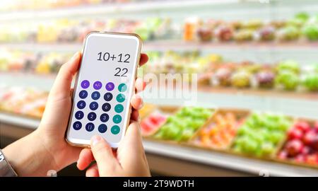 Calculator on mobile phone screen in customer's hands. Young woman does accounts in the supermarket using calculator. Stock Photo