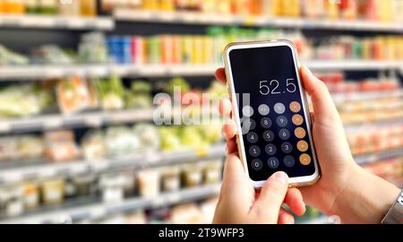 Calculator on mobile phone screen in customer's hands. Young woman does accounts in the supermarket using calculator. Stock Photo