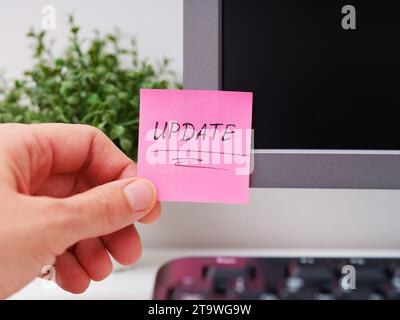 A person hand sticking a pink paper notes with the reminder Update on to a monitor at an office workplace. Stock Photo