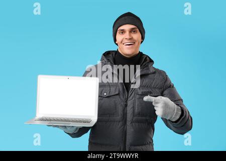 Young man in stylish puffer jacket with modern laptop on blue background Stock Photo
