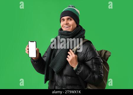Young man in stylish puffer jacket with mobile phone and bag on green background Stock Photo