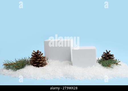 Decorative podiums with Christmas tree branches and pine cones on snow against blue background Stock Photo