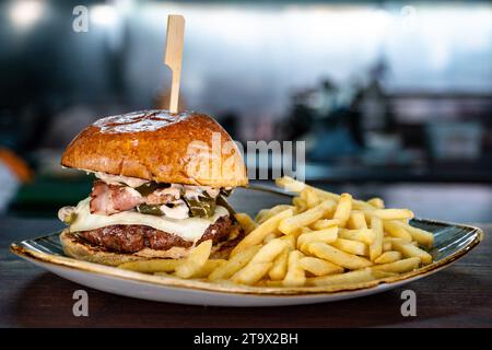 a grilled angus cheeseburger filled with bacon and served with French fries. Stock Photo