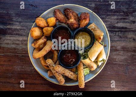a birds eye view of a plate of deep fried appetizer combo served with various dipping sauces. Stock Photo