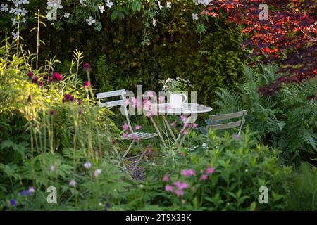 secluded garden seating area in the shade with metal cafte style table and chairs and jug of flowers - UK Stock Photo