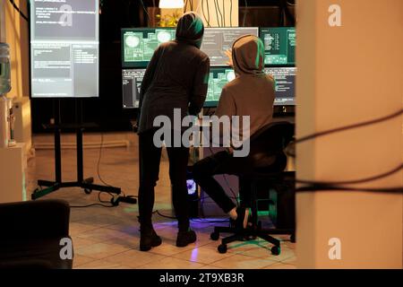 Team of cybercriminals cracking server encryption and hacking system, working on cyberterrorism at night. Young hackers doing criminal activity, stealing sensitive information. Stock Photo