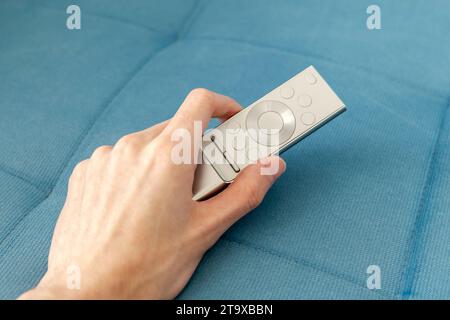Man picking up holding a modern silver smart TV remote in his hand on a couch, sofa watching television, online video streaming smart TV equipment and Stock Photo