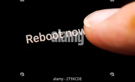 Man hand finger pressing the reboot now computer restart button on a touch screen display rebooting a smartphone, tablet mobile phone device, macro de Stock Photo