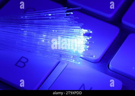 Optical fiber strands transmitting blue light on computer keyboard, macro view Stock Photo