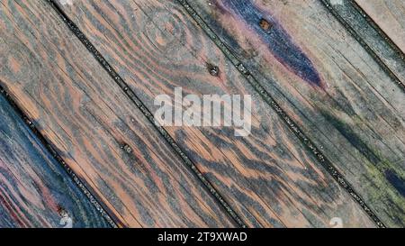 Background of wooden surface made of boards with multicolored spots from humidity, diagonal lines, top view, close-up. Stock Photo