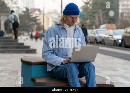 Hipster guy freelancer working on laptop outdoors, man student sitting outside checking email Stock Photo