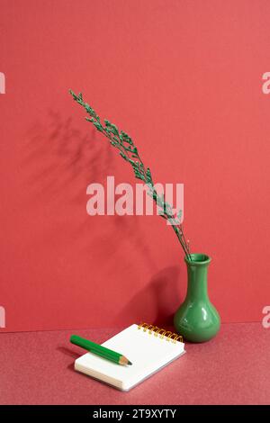 Notepad and colored pencil with vase of plant on red desk. red wall background, workspace Stock Photo
