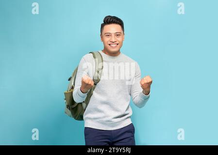 Portrait of happy excited young Asian tourist backpacker man raising his fists doing success gesture Stock Photo