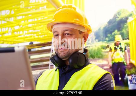 Cheerful caucasian worker smiling wearing a yellow hardhat looking a tablet . Stock Photo