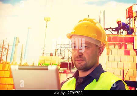 Construction worker that is uniform and hard hat is standing and using tablet Stock Photo