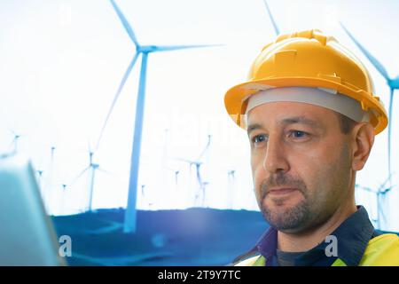 Male engineer working and writing on a clipboard against wind turbine farm. Stock Photo