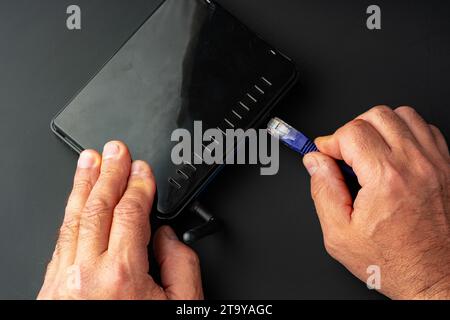 Man's hand plugging internet cable into wifi router Stock Photo