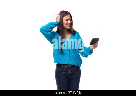 charming caucasian woman with black hair dressed in a blue cardigan watches attentively the video on the smartphone. e-business concept Stock Photo