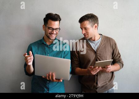 Young manager talking with experienced colleague while using computer in office. Stock Photo