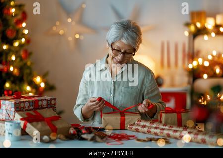 Merry Christmas and Happy Holidays. Cheerful pretty senior woman preparing  presents. Stock Photo